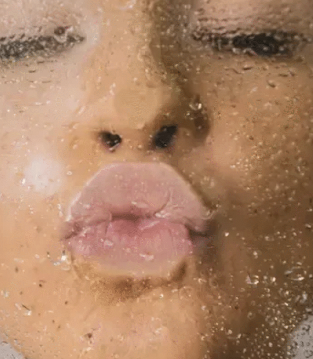 Kvinna som gör pussmun på en våt duschvägg.