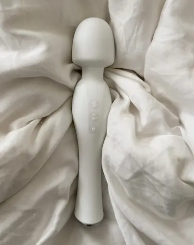 Vit vibrator ligger bland vita sängkläder.
