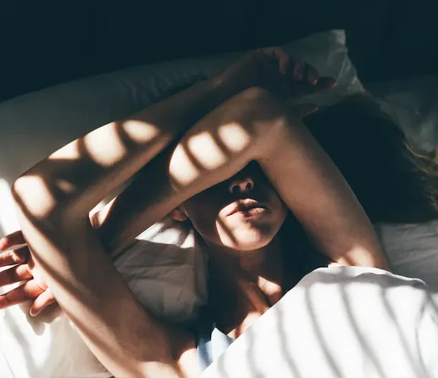 Kvinna som ligger i sängen med armen över ansiktet och vilar.