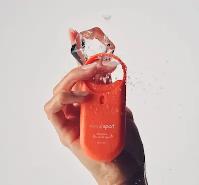 Hand som håller en orange, liten flaska och en istbit.