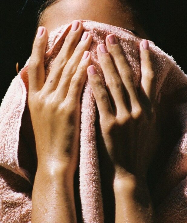 En kvinna som torkar sig i ansiktet med en rosa handduk.