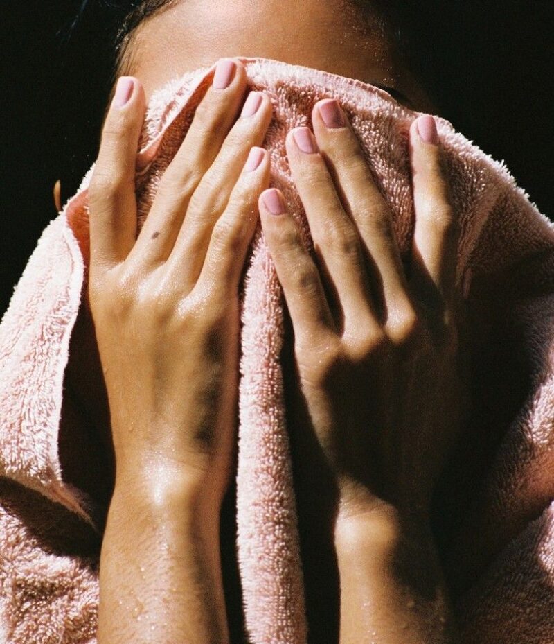 En kvinna som torkar sig i ansiktet med en rosa handduk.