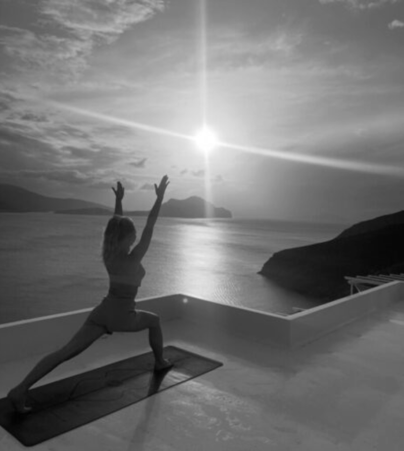 Kvinna som stretchar i solnedgången, vid havet.