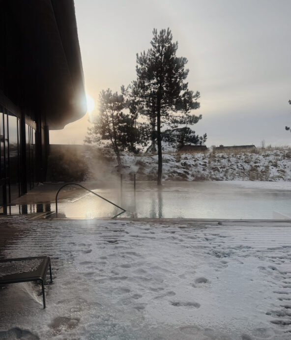 Lanserhofs poolområde. det är vintrigt och disigt och från poolen stiger imma då det är kallt i luften och varmt i vattnet. Der är vacker utsikt med tallar och snö i förgrunden.