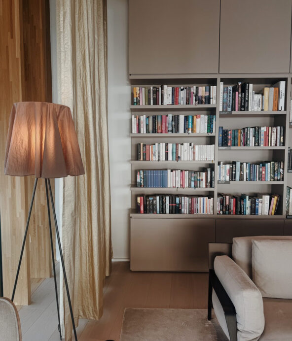 Bokhylla fylld med böcker. Soffa och en läslampa i förgrunden.