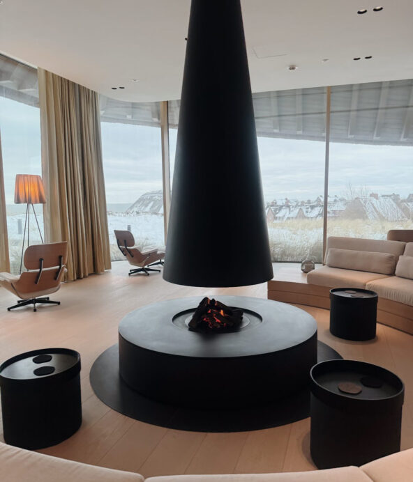 Gemensamt utrymme på Lanserhof. Ljusa soffor och en stor, rund eldstad i mitten med en trattformad svart skorsten.