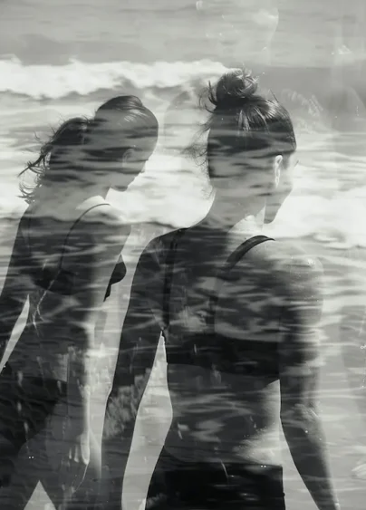 Två kvinnor som går på stranden, svartvit bild.