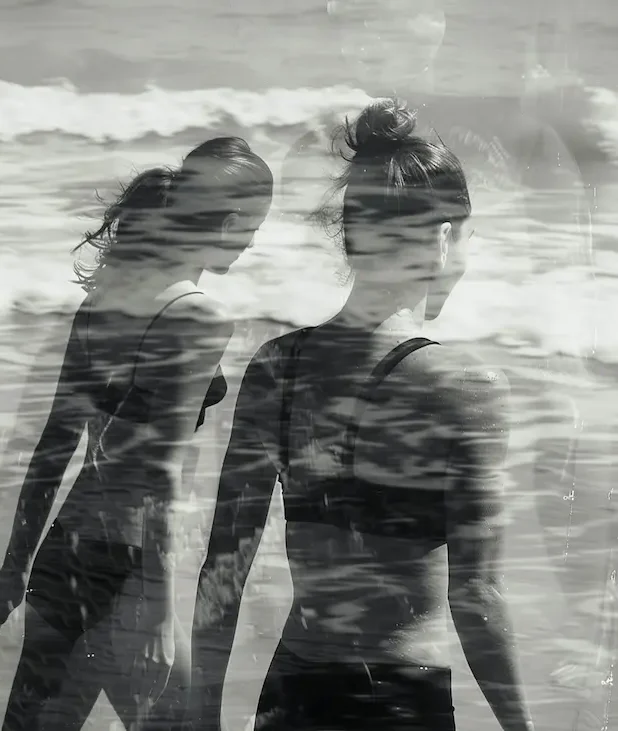 Två kvinnor som går på stranden, svartvit bild.