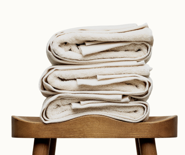 En hög med ljust beiga frottéhanddukar från Reboco. Handdukarna ligger på en bru träpall.