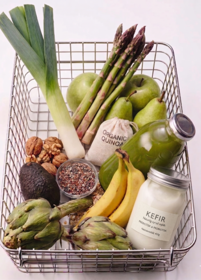 Varukorg fylld med fiberrik mat som sparris, avokado, kronärtskocka och banan.