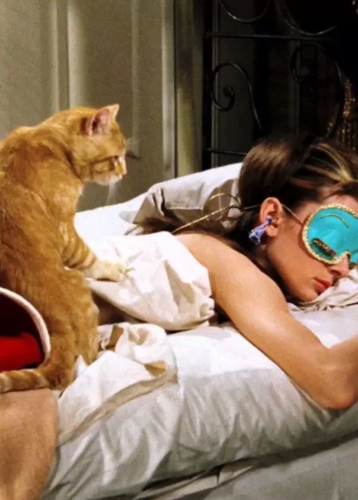 Audrey Hepburn från filmen "Breakfast in Tiffany's". Hon ligger i sängen med sovmask över ögonen och hennes katt sitter bredvid på sängen och tittar när hon sover.