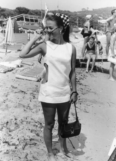 Natalie Wood fotad på stranden i St Tropez 1968, svartvit bild. Nathalie har vit klänning, solglasögon, handväskan och scarf på huvudet.
