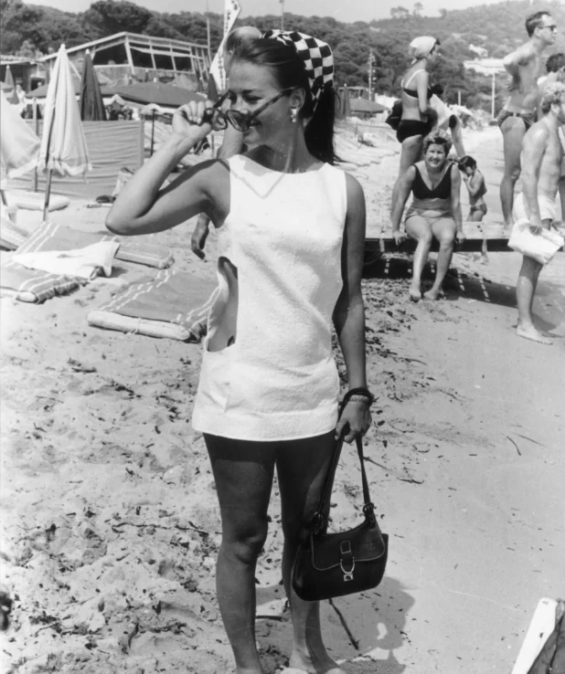 Natalie Wood fotad på stranden i St Tropez 1968, svartvit bild. Nathalie har vit klänning, solglasögon, handväskan och scarf på huvudet.