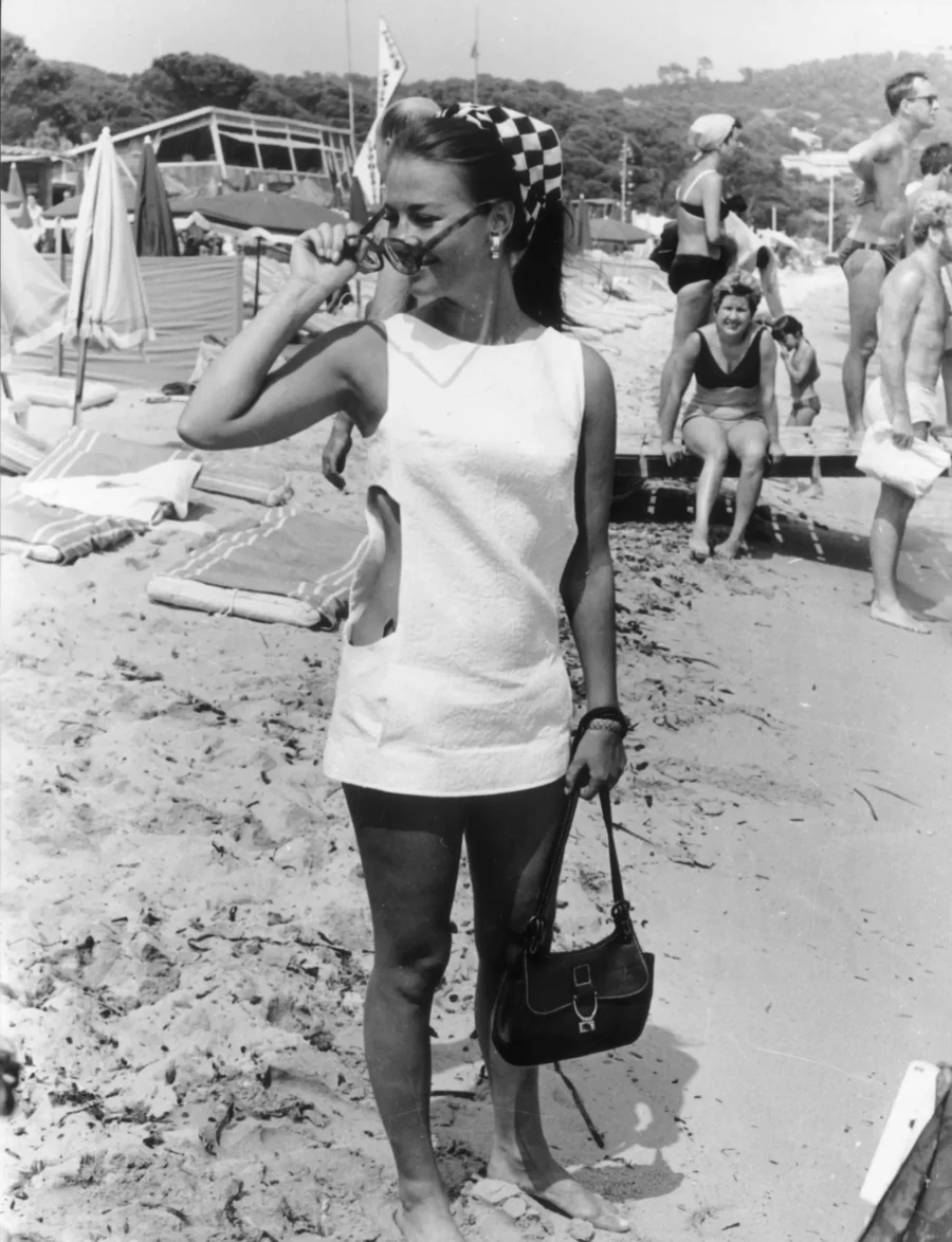 Natalie Wood fotad på stranden i St Tropez 1968, svartvit bild. Nathalie har vit klänning, solglasögon, handväskan och scarf på huvudet.